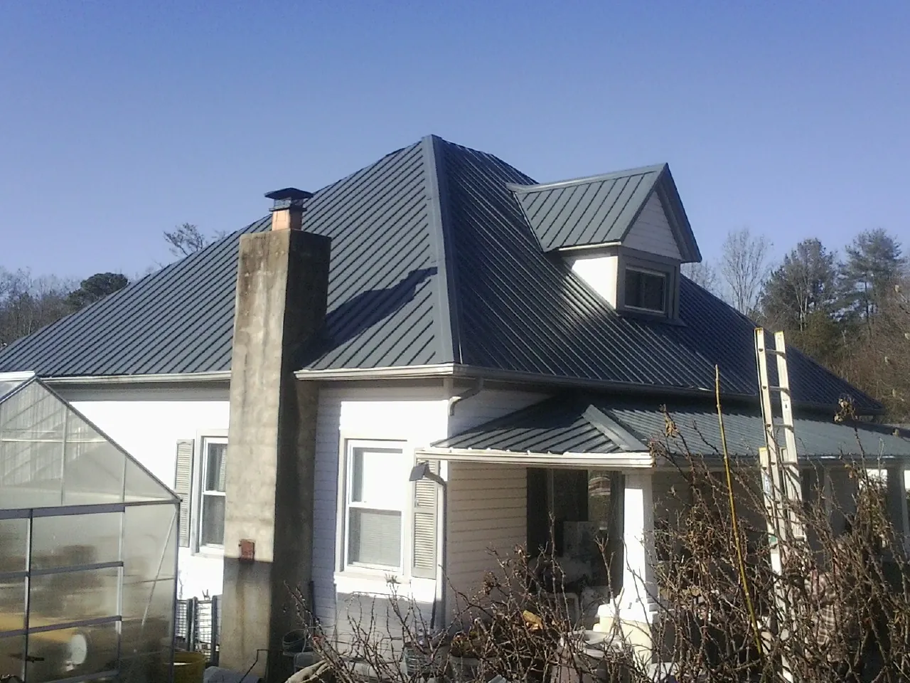 Dark blue standing seam metal roof on a white farmhouse with dormer — Slate & Tile Roof Repair by Roofing Brothers in Diberville