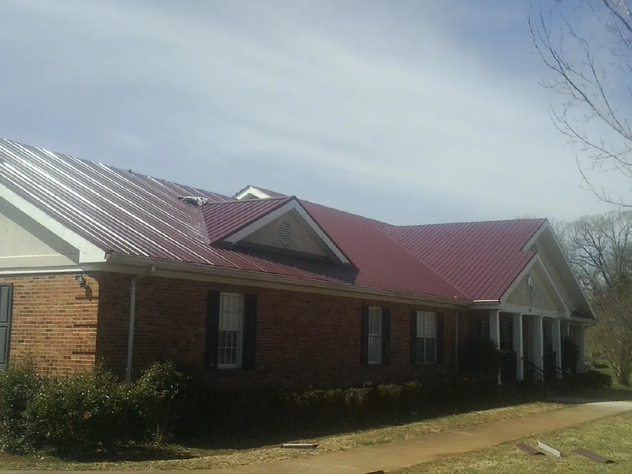 Red metal roof with gabled entries on a long brick building, from a Hail Damage Roof Repair job in Diberville