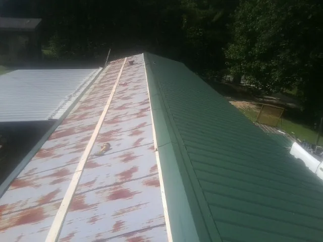 Old rusted panels beside newly installed green metal roofing — Wind Damage Roof Repair by Roofing Brothers in Diberville