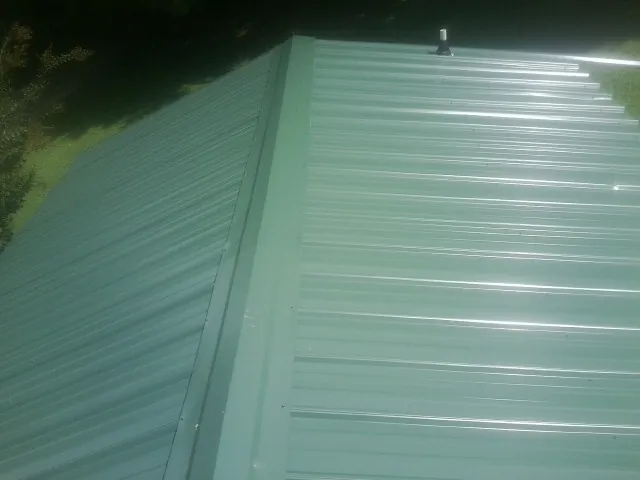 New green metal panels meeting at the ridge of a roof — Flat Roof Repair work by our crew in Diberville