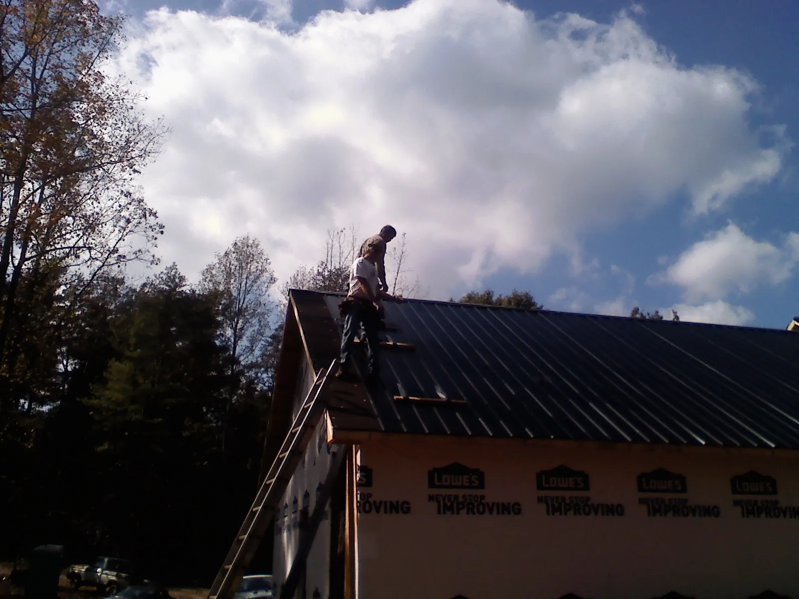 Roofer fastening dark metal panels high against a cloudy sky, from a Roof Inspection job in Diberville