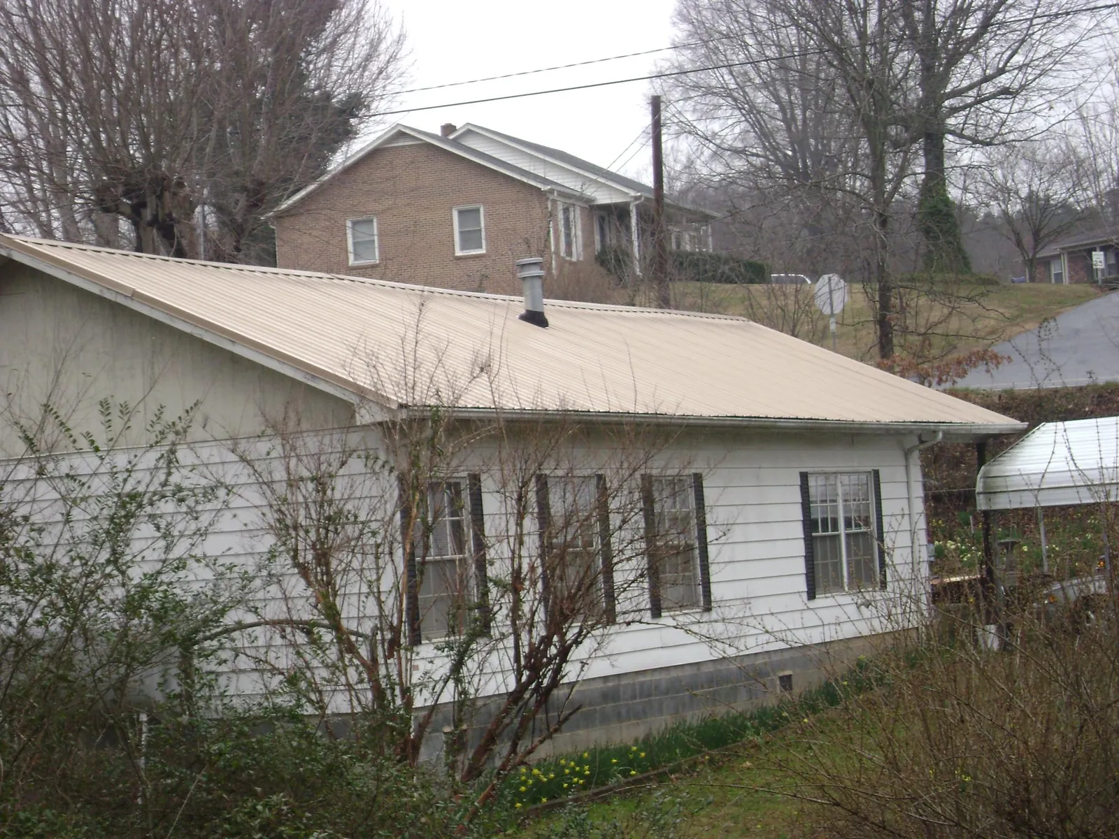 Tan metal roof on a white sided house set into a hillside — Commercial Roofing by Roofing Brothers in Diberville