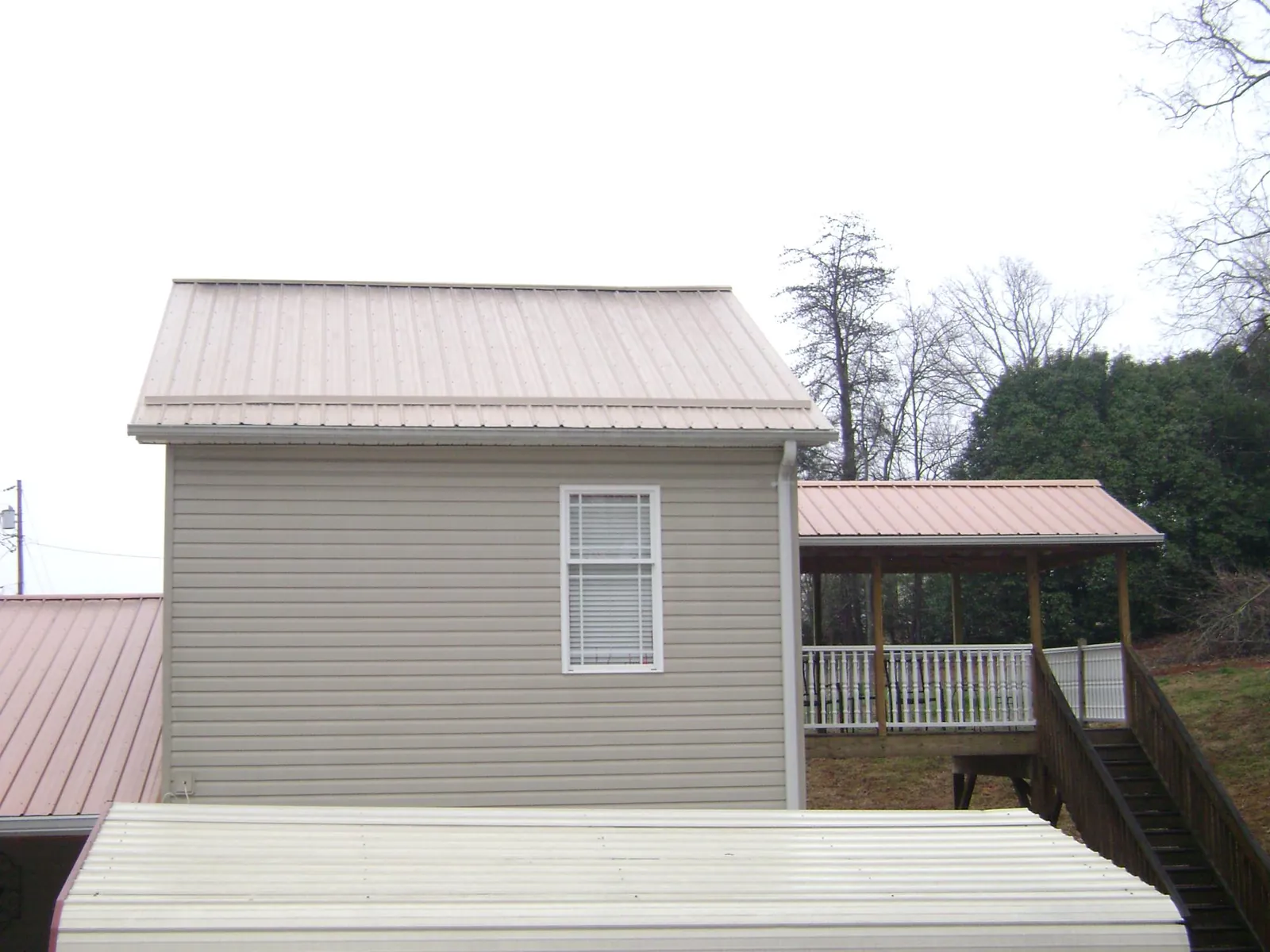 Tan metal roofs on a two story addition and attached porch, from a Roof Replacement job in Diberville
